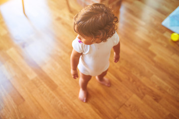 Beautiful toddler child girl wearing white t-shirt standing on the floor using pacifier