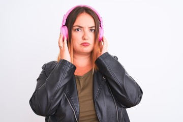 Young beautiful woman listening to music using headphones over isolated white background with serious expression on face. Simple and natural looking at the camera.