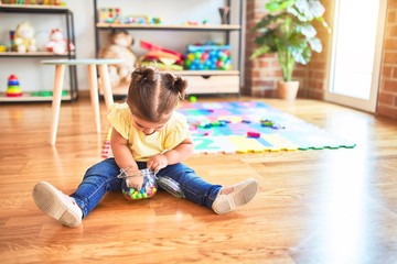 Beautiful toddler sitting on the floor with jar of chocolate colored balls at kindergarten