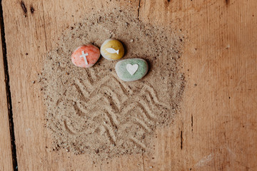 Kommunion, Konfirmation, Firmung, Taufe - bunte Steine mit Kreuz, Herz und Fisch auf Sand und Holz