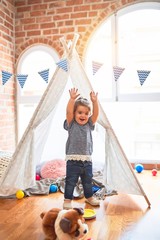 Beautiful toddler standing inside tipi with hands raised smiling at kindergarten