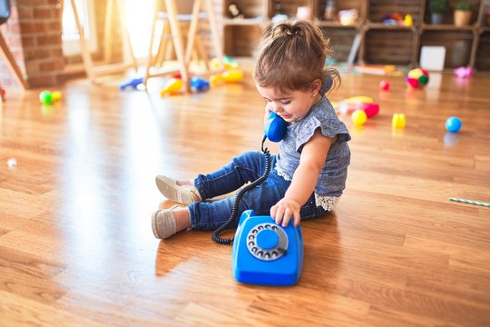 Beautiful toddler sitting on the floor playing with vintage phone at kindergarten