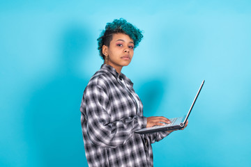 young african american woman with blue curly hair and laptop computer isolated on yellow background