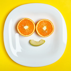 Top view of the two orange and one apple slice at the white dish making a smile, while lies on the...