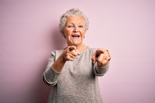 Senior beautiful woman wearing casual t-shirt standing over isolated pink background pointing to you and the camera with fingers, smiling positive and cheerful
