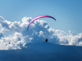 Man on a paraglider over the mountains against the background of clouds and blue sky