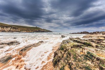 Tagle beach in winter with dramatic sky and waves against the rocks
