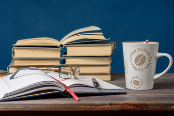 Open notebook, glasses, pencil, books and a cup of coffee on a wooden table. Preparation for classes.