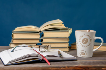 Open notebook, glasses, pencil, books and a cup of coffee on a wooden table. Preparation for classes.
