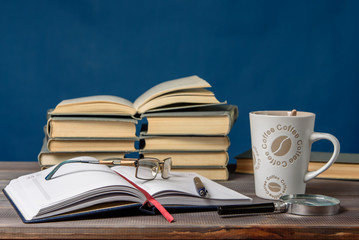 Open notebook, glasses, pencil, books and a cup of coffee on a wooden table. Preparation for classes.