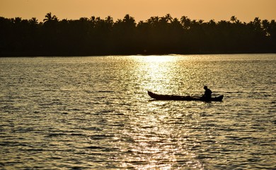 Lone fisherman at the dusk and sunset sails through the coast