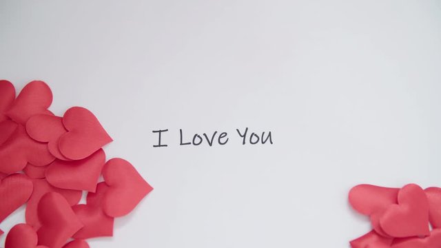 Hearts blown away reveal message I Love You in slow mov 4K. Valentine gift message with pile of hearts covering a text message in focus. 