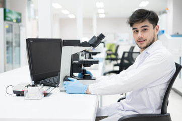 Portrait scientist man sitting and looking microscope in laboratory.Researcher using microscope in medical laboratory. Medical healthcare technology and pharmaceutical research concept.