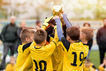 Happy kids in yellow shirts in elementary school sports team celebrating soccer succes in...