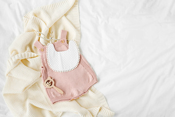 Pink bodysuit and  bib on knitted blanket. Set of  kids clothes and accessories  on bed. Fashion...