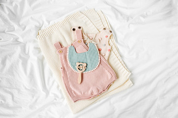 Pink bodysuit and  bib on knitted blanket. Set of  kids clothes and accessories  on bed. Fashion...