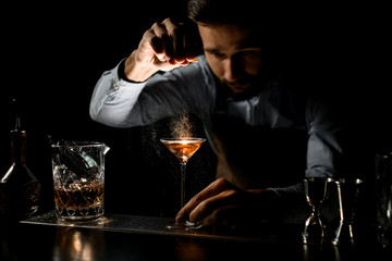 Bartender spraying on the alcoholic drink in a martini glass with orage zest juice