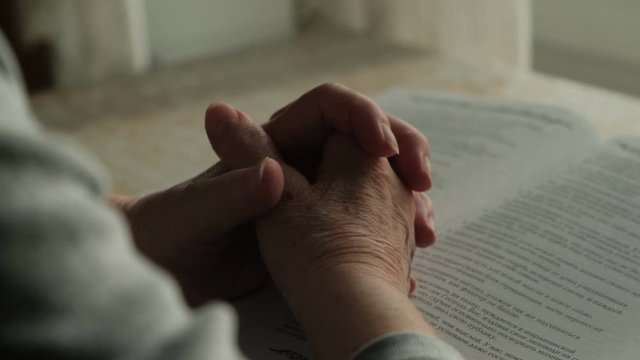 An old woman prays with her hands on the bible, close-up