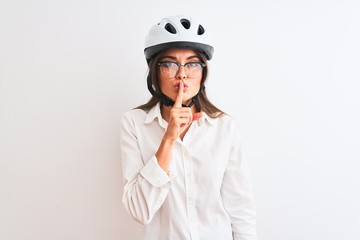 Beautiful businesswoman wearing glasses and bike helmet over isolated white background asking to be quiet with finger on lips. Silence and secret concept.