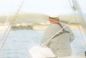 Yachtsman in marine clothing looking into the distance sitting on board a sailing yacht. Sea fishing from the ship. Peaceful state at summer holidays. Travel experienced person around the world