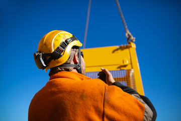Trained rigger wearing safety helmet, orange long sleeve shirt using two way radio communicating...