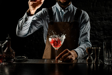 Bartender throwing a red rose bud to a martini glass with a golden cocktail