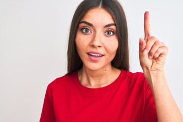 Young beautiful woman wearing red casual t-shirt standing over isolated white background surprised with an idea or question pointing finger with happy face, number one