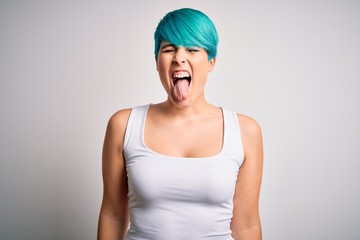 Young beautiful woman with blue fashion hair wearing casual t-shirt over white background sticking tongue out happy with funny expression. Emotion concept.