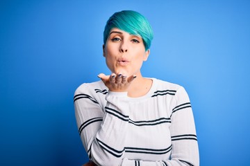 Young beautiful woman with blue fashion hair wearing casual sweater standing at studio looking at the camera blowing a kiss with hand on air being lovely and sexy. Love expression.