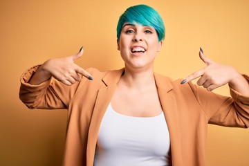 Young beautiful woman with blue fashion hair wearing casual jacket over yellow background looking...