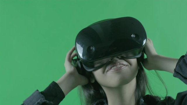 Young woman listen music and dancing in the VR headset. Virtual reality helmet on the green background. Chroma Key