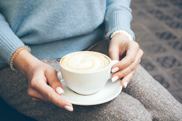 People and leisure.  Close up of woman hands with manicure holding cup of coffee, dressed in trendy blue sweater is enjoying hot drink. Having rest in a cafe, drinking cappuccino,  relaxing