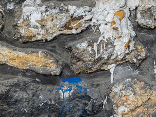 wall of large multicoloured stones with large streaks of paint and cement around it