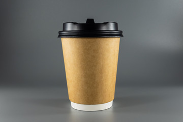 Disposable paper Cup for hot coffee or tea. A brown Cup with a black lid on a gray background. Cup of the Kraft paper