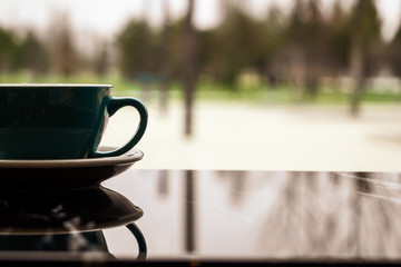 A Cup of coffee with a reflection in a cozy coffee shop. A Cup and saucer stand on a table with a copy space on the background of the window. Warming drink after a walk in cold weather