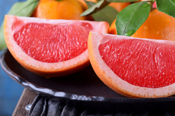 Slices of red grapefruit and whole mandarins with green leaves on the black plate