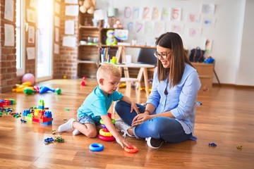 Fototapeta premium Young caucasian child playing at playschool with teacher. Mother and son at playroom with intelligence toy