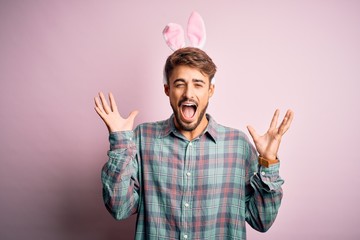 Young handsome adult man wearing cute easter rabbit ears over pink isolated background celebrating...