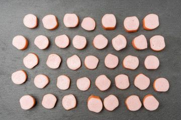 Put in row many pieces of fresh pork sausages of different sizes on stone board, cut for frying and adding to soup. Meat product. Semimanufactures. View from top