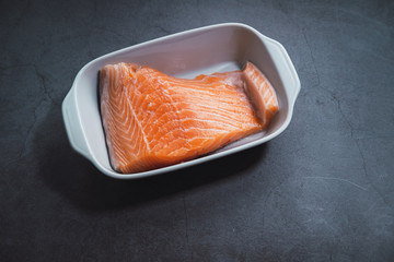 Raw salmon fillet on white tray and concrete background.
