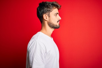 Obraz premium Young handsome man with beard wearing casual t-shirt standing over red background looking to side, relax profile pose with natural face with confident smile.