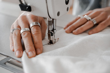 Men's hands near the sewing machine hold a white cloth, in the process of sewing, a seam. Sewing, design work, tailoring studio, tailor, designer clothes, manufactory, in the process of creative work