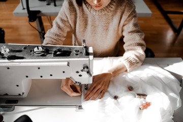 Woman seamstress at the sewing machine focused on sewing. Sewing, design work, tailoring studio, tailor, designer clothes, manufactory, in the process of creative development - obrazy, fototapety, plakaty