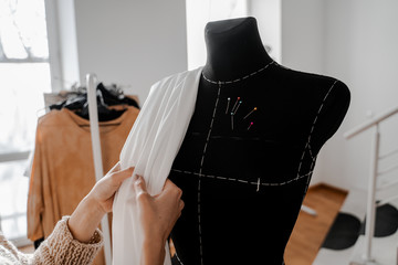 Hands that sort through the fabric. Mannequin with fabric on the shoulder and stuck pins into the...