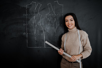 Beautiful educated seamstress of the highest qualification conducts a training course in tailoring. Drawing of a pattern on a blackboard in a design studio for sewing and tailoring, special education