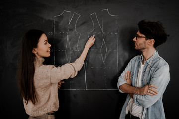 Two professional tailors man and woman create new drawings patterns for new collection of clothes. Drawing of a pattern on a blackboard in a design studio for sewing and tailoring, special education