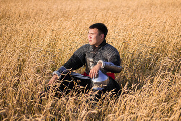 Naklejka na ściany i meble Asian warrior in oriental armor and with a saber in his hands sitting in a wheat field