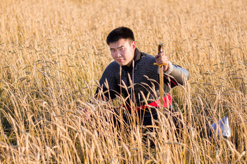 Naklejka na ściany i meble Asian warrior in oriental armor and with a saber in his hands sitting in a wheat field