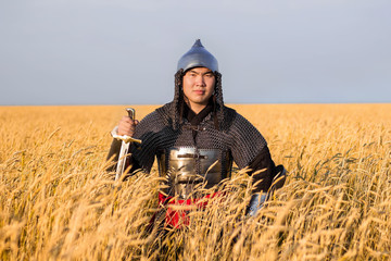  Asian warrior in oriental armor and with a saber in his hands sitting in a wheat field