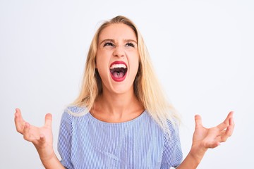 Young beautiful woman wearing elegant blue t-shirt standing over isolated white background crazy and mad shouting and yelling with aggressive expression and arms raised. Frustration concept.